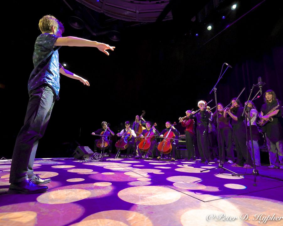 En person på scenen med mikrofon og en gruppe mennesker