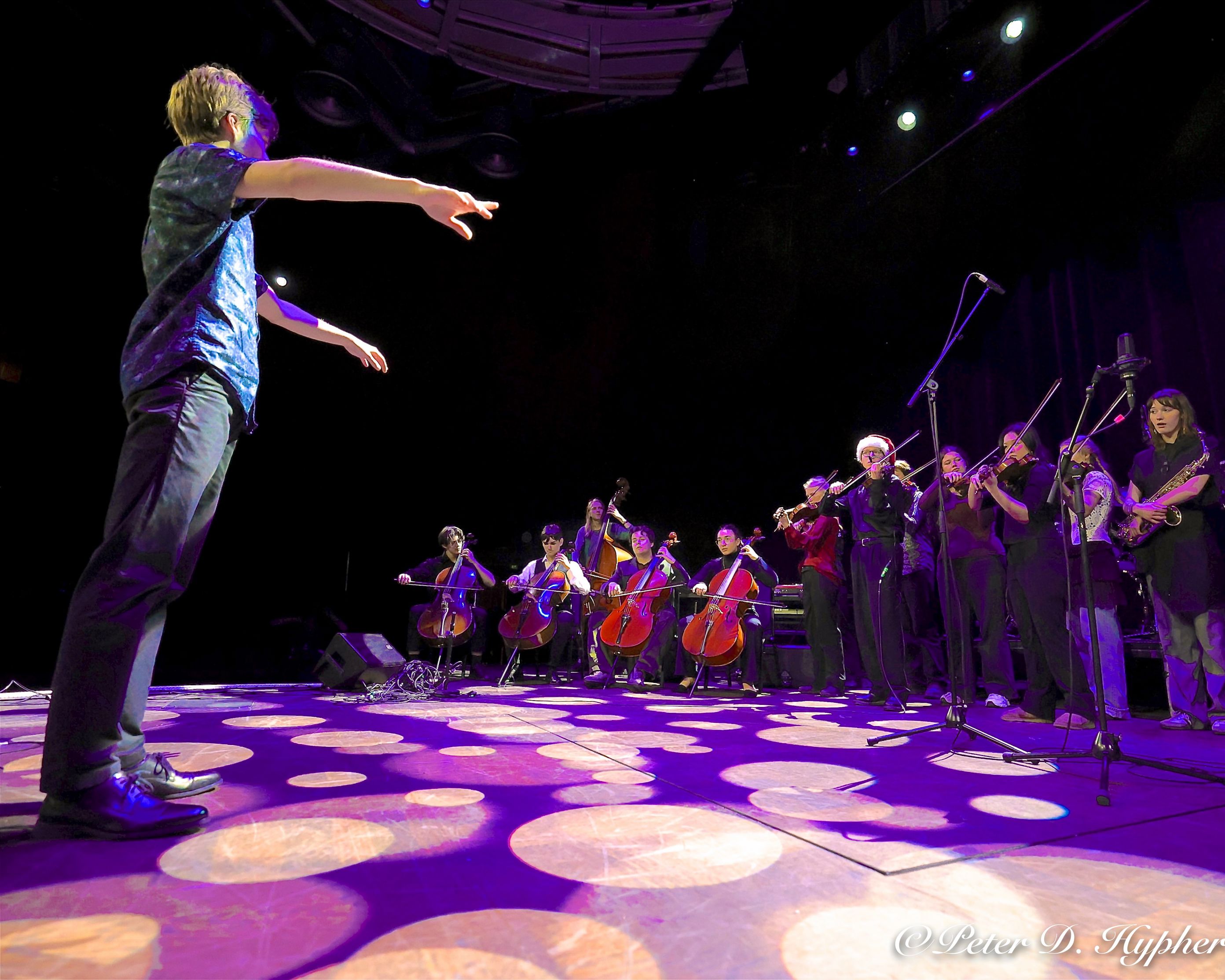 En person på scenen med mikrofon og en gruppe mennesker En person på scenen med mikrofon og en gruppe mennesker