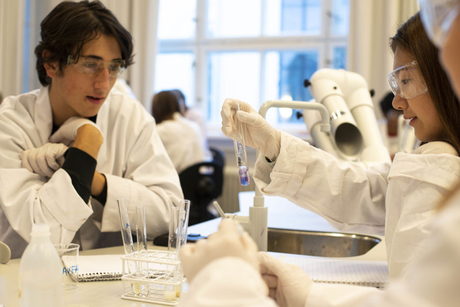 en person og en person i laboratoriefrakker som ser på et mikroskop